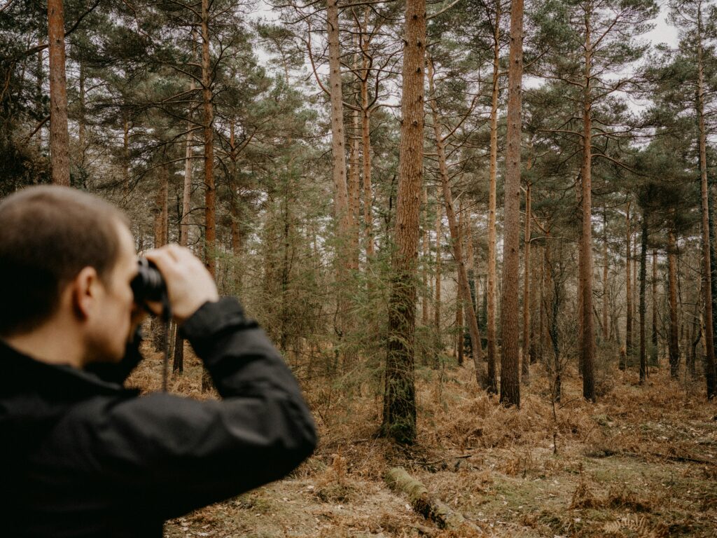man with binoculars and forest behind him