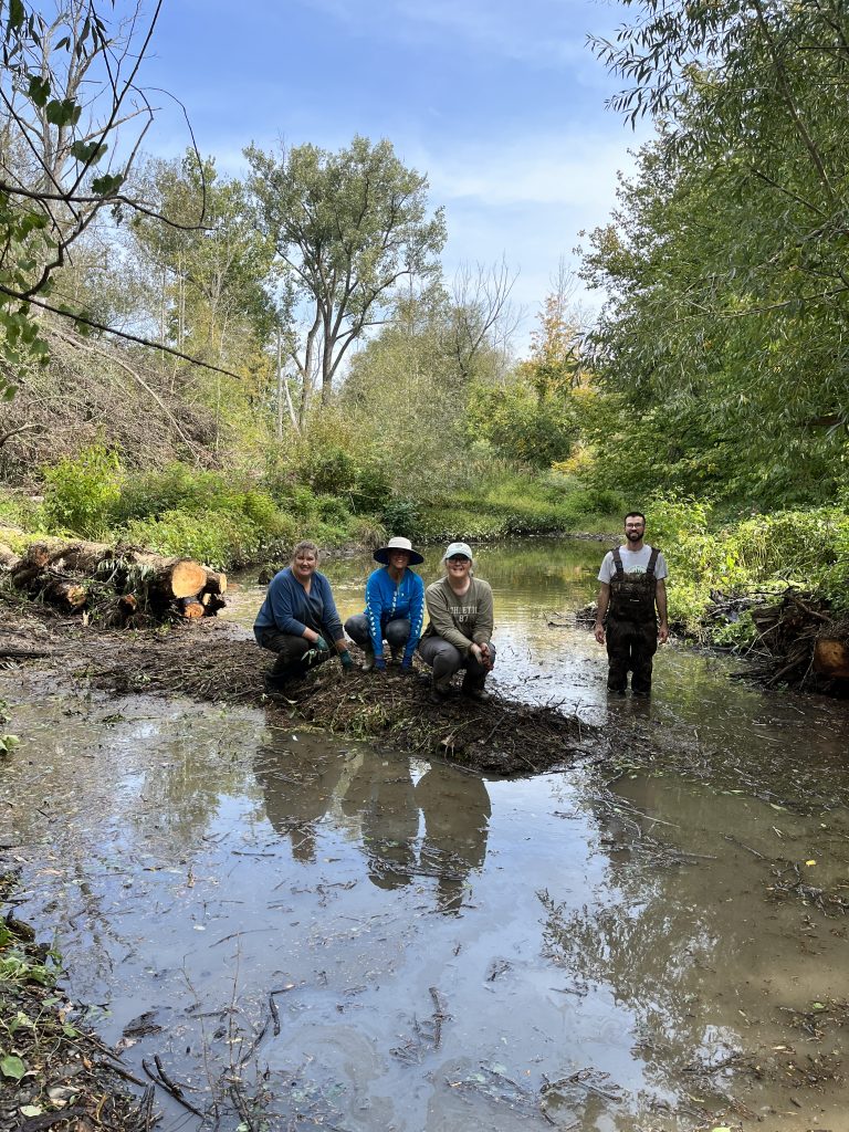 Four people crouching and standing amid water in nature