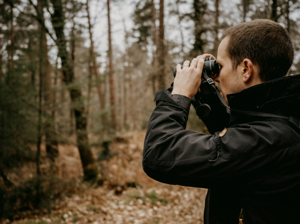 man holding binoculars with woods in background