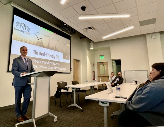a man (Sean Ryan) stands at a podium in a room with "The Bird-Friendly City" written on a PowerPoint in the background