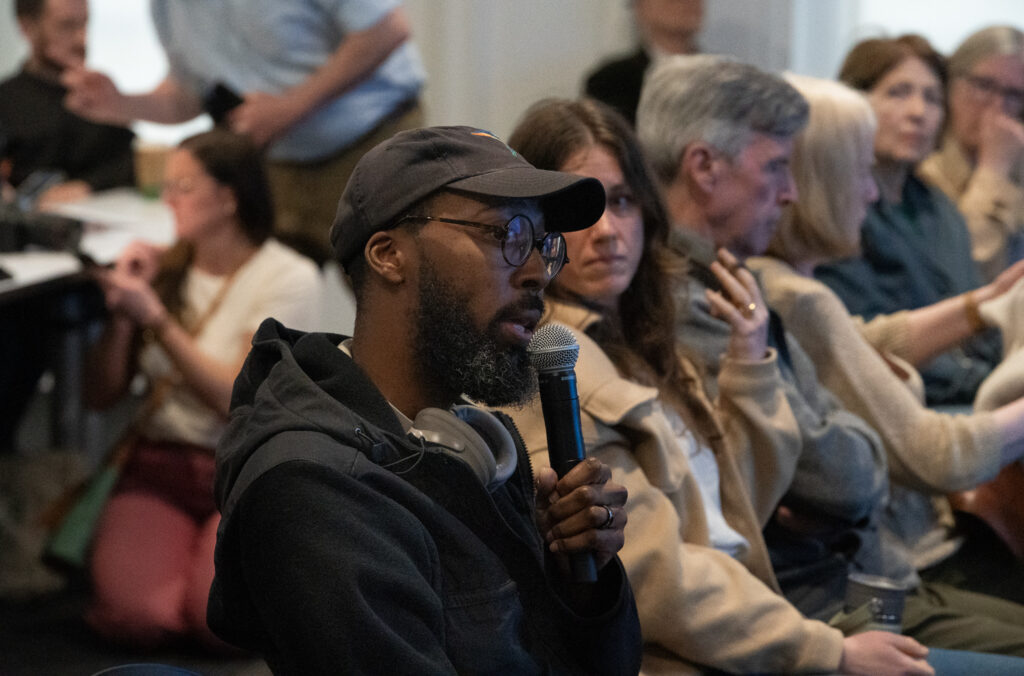 man speaking into microphone surrounded by others in audience at bird-friendly symposium